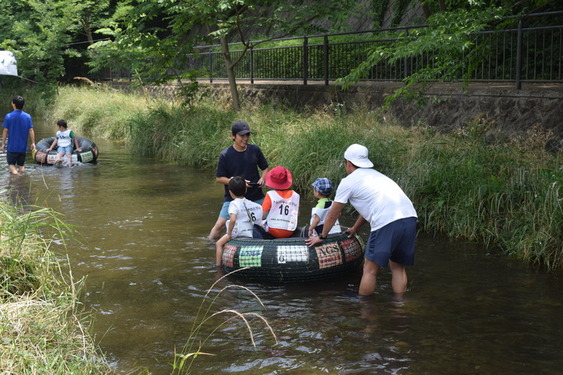 落合川でタイヤチューブに乗って川下りをする子供たちの様子